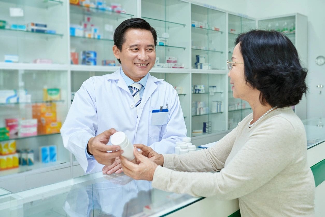 A woman is handing a medicine to a pharmacist.