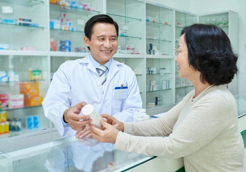A woman is handing a medicine to a pharmacist.