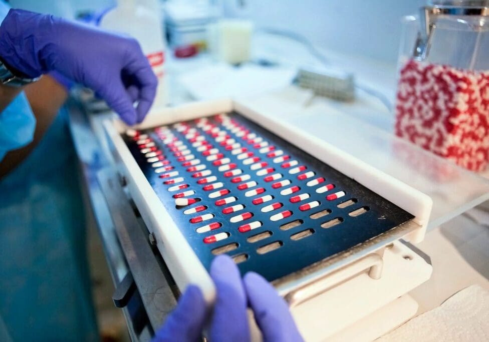 A person in blue gloves is working on a tray of pills.